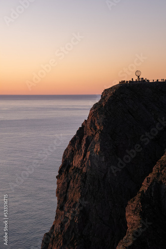 Wonderful landscapes in Norway. Nord-Norge. Beautiful scenery of a midnight sun sunset at Nordkapp (Cape North). Boat and globe on a cliff. Rippled sea and clear orange sky. Selective focus photo