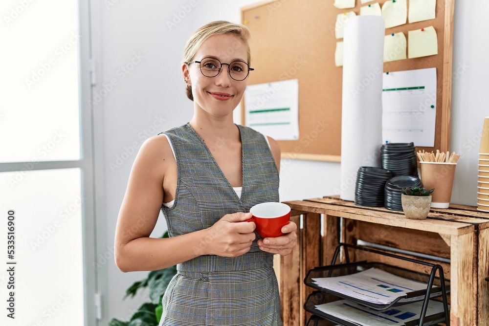 Young caucasian woman smiling confident drinking coffee standing at office Young caucasian woman smiling confident drinking coffee standing at office