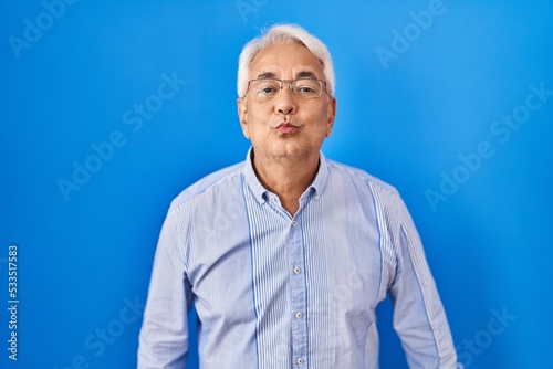 Hispanic senior man wearing glasses looking at the camera blowing a kiss on air being lovely and sexy. love expression.