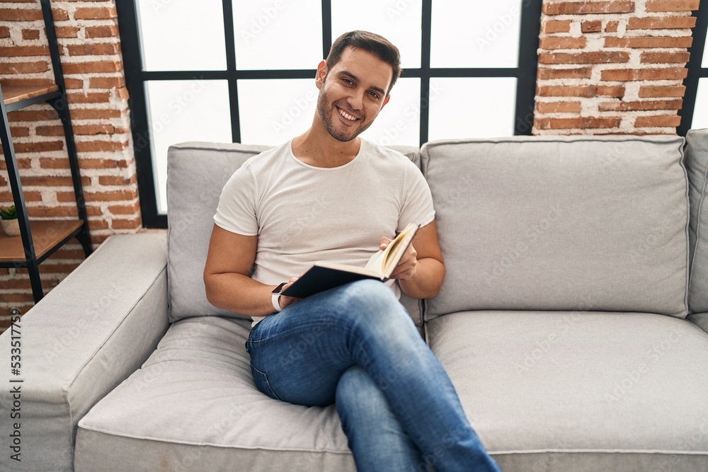 Young hispanic man reading book sitting on sofa at home Young hispanic man reading book sitting on sofa at home