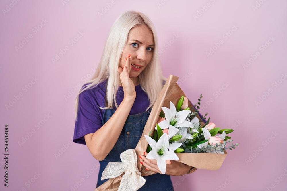 Caucasian woman holding bouquet of white flowers hand on mouth telling secret rumor, whispering malicious talk conversation