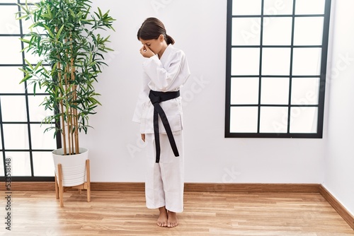 Young hispanic girl wearing karate kimono and black belt tired rubbing nose and eyes feeling fatigue and headache. stress and frustration concept.