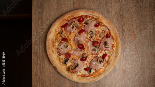 Italian pizza with cheese, ham, cherry tomatoes, onions and mushrooms on the table background