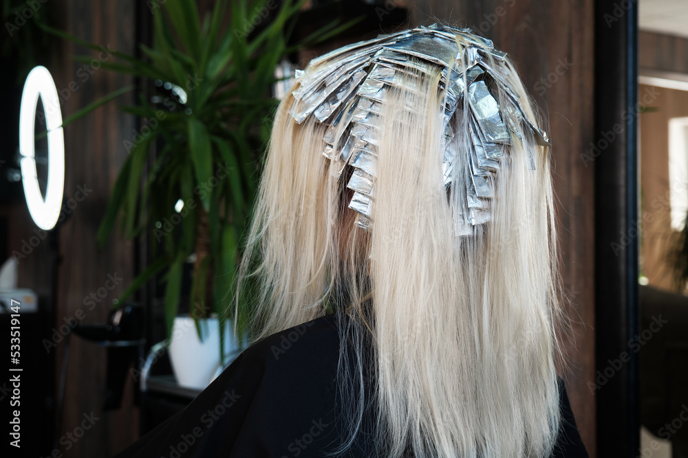 Young woman in a hairdressing salon dyes her hair blond