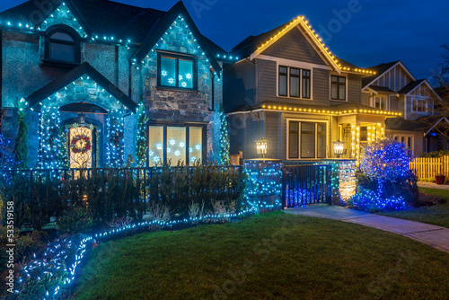 Two story stucco luxury house with garage door, big tree and nice Christmas decoration at night in Vancouver, Canada, North America. Night time on Dec 2021.