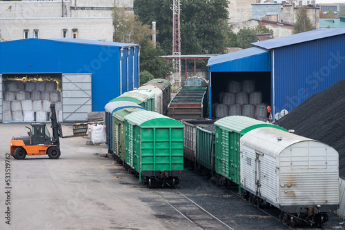 Modern train with shipping containers transporting necessary materials for logistic import export operations in dull morning. Loader for containers with coal in railway station terminal by buildings