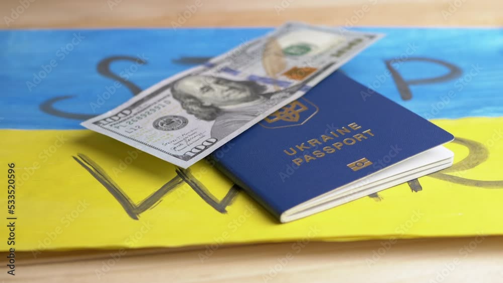 Hand Puts a Biometric Passport of Ukraine with Cash on a Background of Flag. Drawing of yellow, blue Ukrainian flag with title stop the war lie on table. Money, bribe. War, migrants, Russian attack.