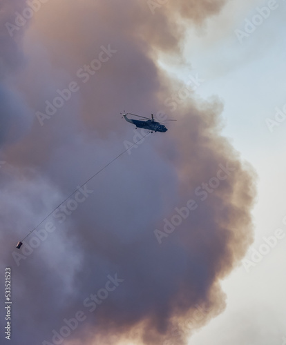 Wildfire Service Helicopter flying over BC Forest Fire and Smoke on the mountain near Hope during a hot sunny summer day. British Columbia, Canada. Natural Disaster