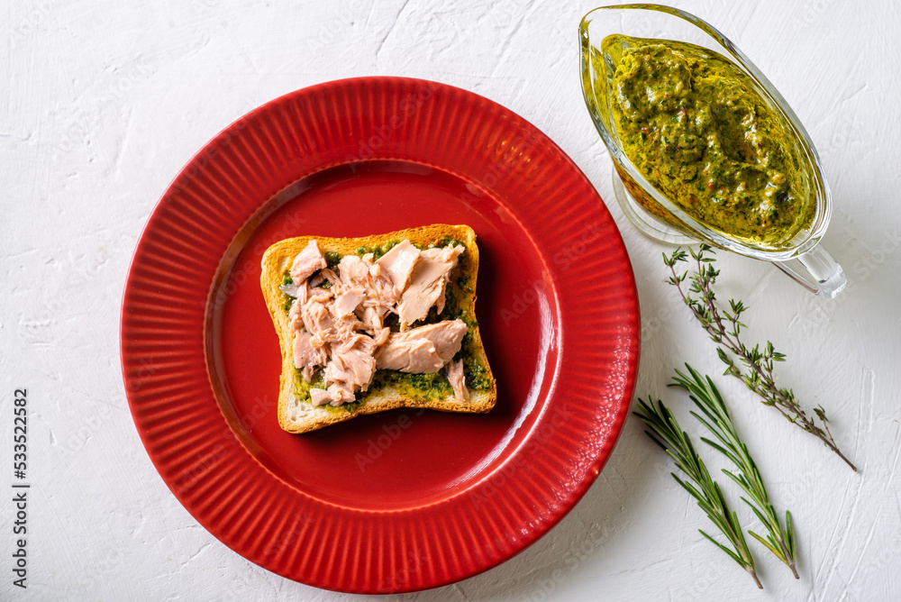 Toast with tuna and chimichurri sauce on a red plate. White background. Toast with tuna and chimichurri sauce on a red plate. White background.