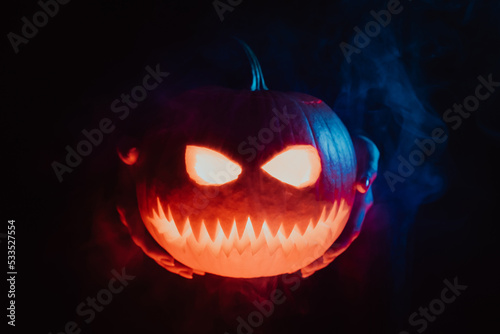 Pumpkin head of jack-o-lantern in hands on black smoke background. Symbol of Halloween, trick or treat. Someone scares you with gourd at night