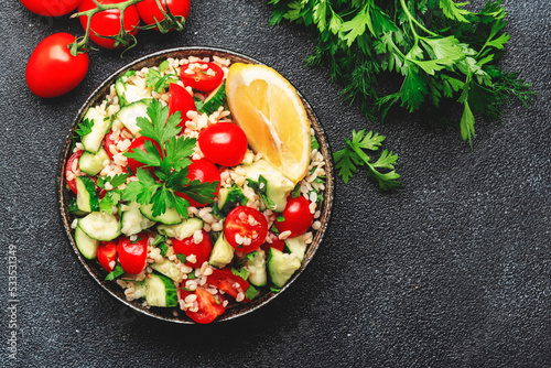 Bulgur tabbouleh salad with fresh tomatoes, cucumbers, parsley and lemon dressing. Traditional Middle Eastern and Arabic dish. Black stone kitchen table background, top view