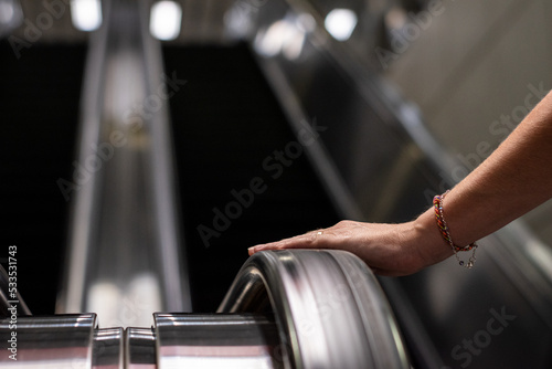 Persona apoyando la mano en baranda de escalera mecánica yendo hacia arriba. Fotografía con enfoque selectivo photo