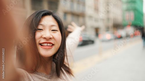 Fotografie, Obraz Asian female blogger smiling while taking self portrait on the street