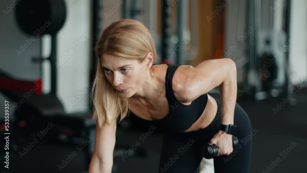 Fitness workout. Focused middle aged sporty woman doing exercises with dumbbells in gym, practicing biceps exercise