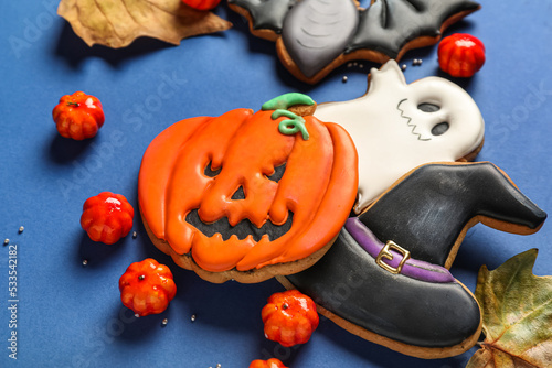 Tasty Halloween cookies, candies and fallen leaves on blue background, closeup