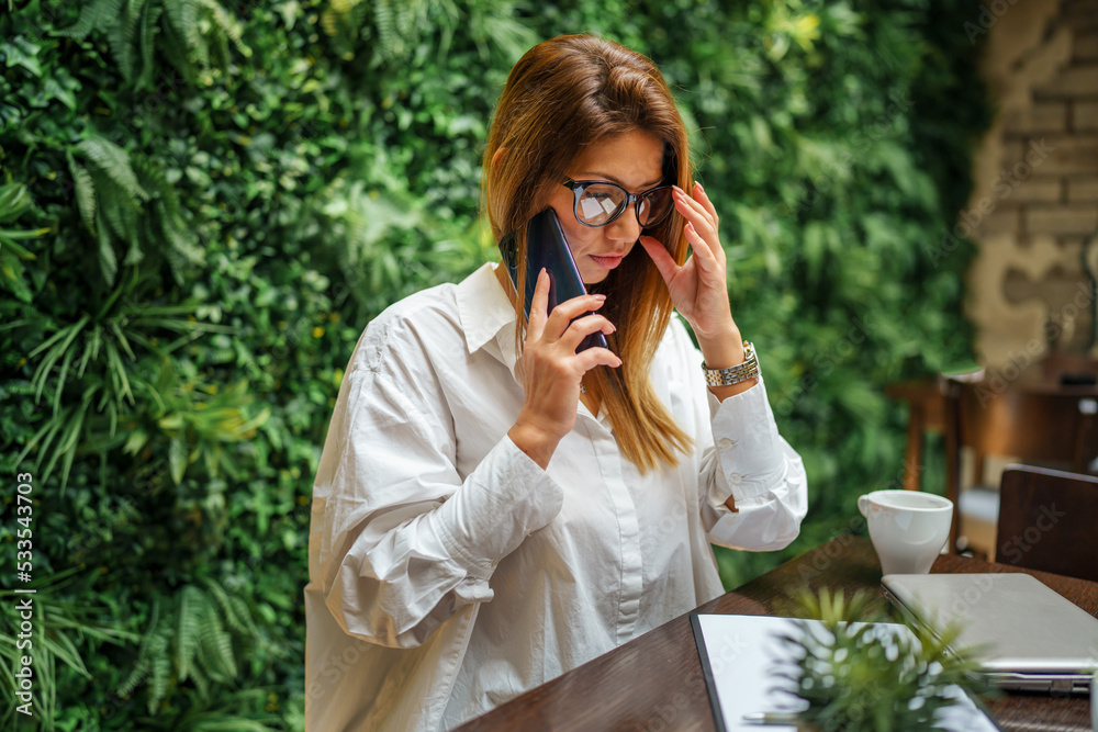 One female young adult caucasian business woman sitting in the restaurant or hotel working and talking on the mobile telephone Entrepreneur manager modern lifestyle concept One female young adult caucasian business woman sitting in the restaurant or hotel working and talking on the mobile telephone Entrepreneur manager modern lifestyle concept