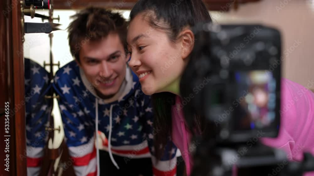 Side view cheerful girl and boy talking filming culinary blog on video camera indoors. Positive happy smiling Asian and Caucasian friends cooking in oven recording vlog in kitchen Side view cheerful girl and boy talking filming culinary blog on video camera indoors. Positive happy smiling Asian and Caucasian friends cooking in oven recording vlog in kitchen