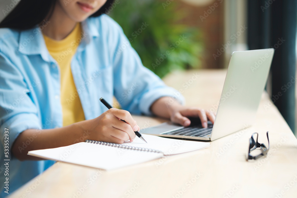 Close up of woman studying, reading book, and taking notes using laptop. Close up of woman studying, reading book, and taking notes using laptop.