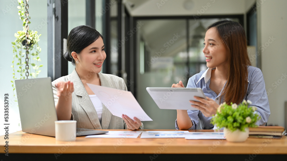 Happy millennial Asian female office employee working, discussing plan with her colleague Happy millennial Asian female office employee working, discussing plan with her colleague