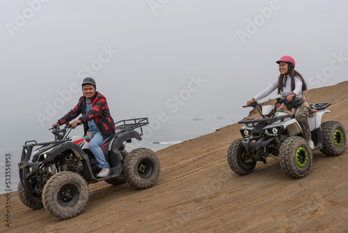 Friends driving quads together in a sandy dune next to the sea