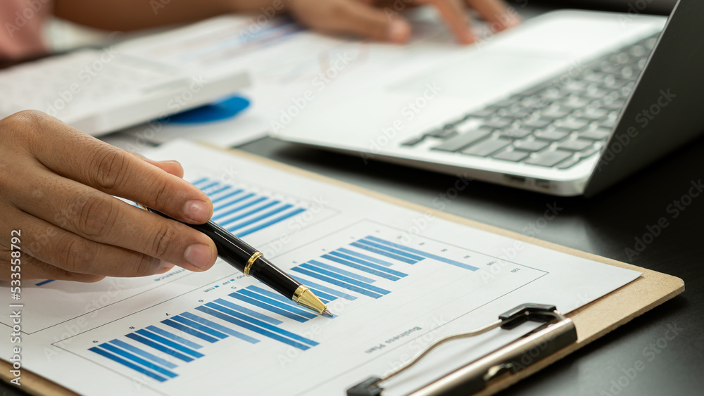 Businessman holding pen pointing to graph while analyzing financial paper graph and on desk at office Businessman holding pen pointing to graph while analyzing financial paper graph and on desk at office