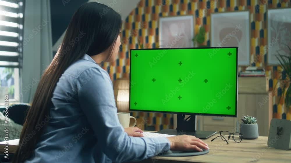 Asian woman sitting at the table and looking at screen of personal computer while surfing the internet in spare time or working remotely from home. Freelance. Green screen and chromakey