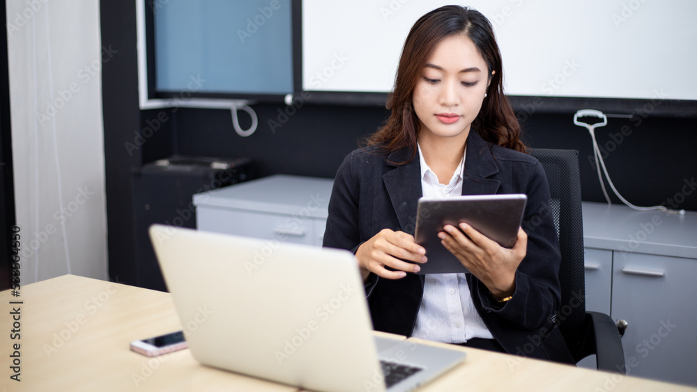 Smiling Asian businesswoman using tablet for work and Cute girl searching for some data and concentrate on her tablet in her office. Smiling Asian businesswoman using tablet for work and Cute girl searching for some data and concentrate on her tablet in her office.
