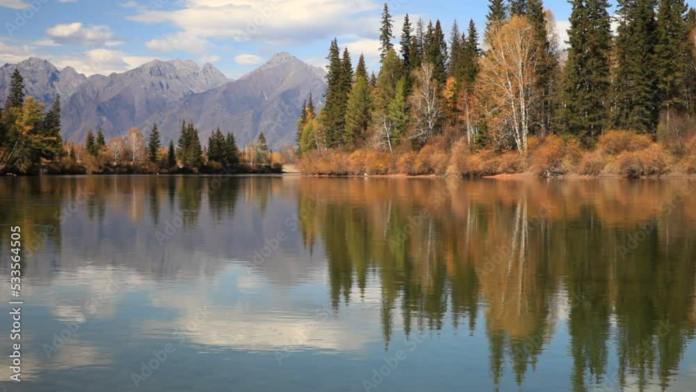 Close-up view of clear water and small ripples of Irkut River with yellowed trees on shore and the mountains of Eastern Sayan in distance on sunny September day. Beautiful autumn calm landscape Close-up view of clear water and small ripples of Irkut River with yellowed trees on shore and the mountains of Eastern Sayan in distance on sunny September day. Beautiful autumn calm landscape