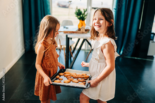 Two kid girls hold tray with fresh cooked cookies in christmas eve for santa at home indoors