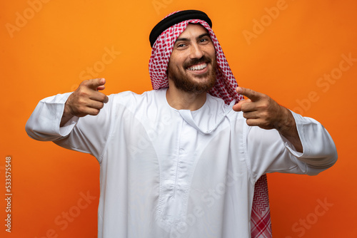 Young Arab man in traditional clothing pointing on you on orange background photo