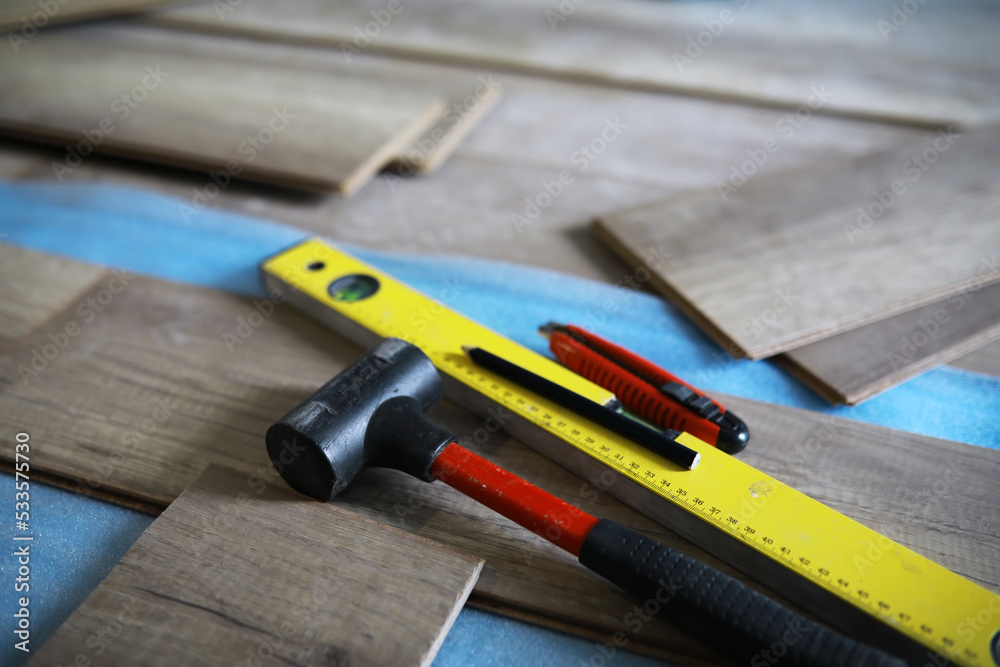 Installing laminated floor, detail on man hands blue wooden tile, over white foam base layer, small pile with more tiles background Installing laminated floor, detail on man hands blue wooden tile, over white foam base layer, small pile with more tiles background