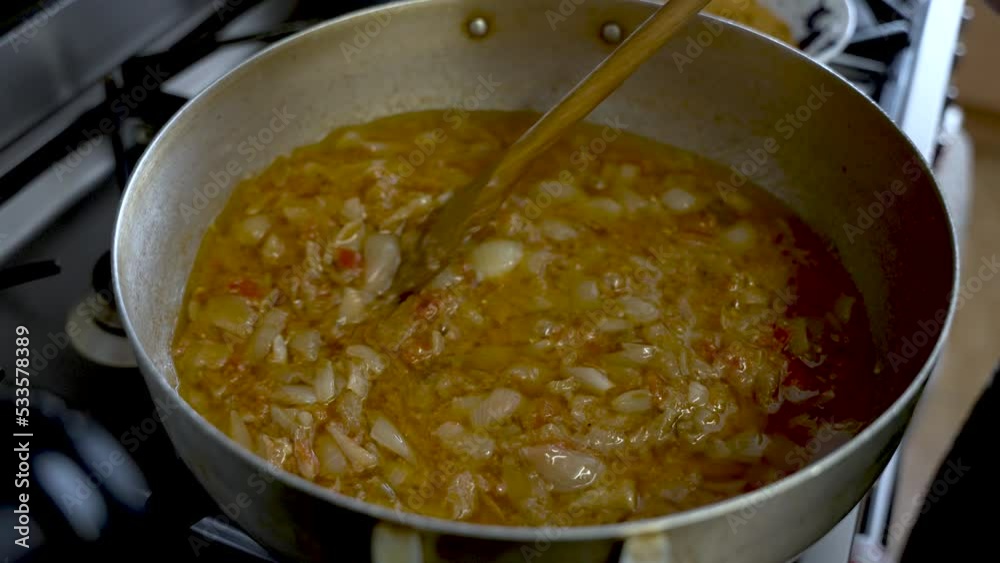 Chopped Onions Being Stirred In Curry Sauce In Large Steel Pot With Wooden Spatula. Slow Motion Chopped Onions Being Stirred In Curry Sauce In Large Steel Pot With Wooden Spatula. Slow Motion