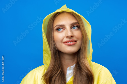 Young blonde woman wearing yellow raincoat smiling at camera over blue background in studio photo