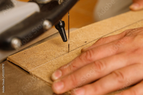 Close-up on the process of sawing wood board on a scroll saw in carpenter workshop.