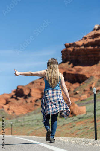 Young woman with long hair walking alone along the highway with her thumb out hitchhiking as a dangerous way to travel and very risky