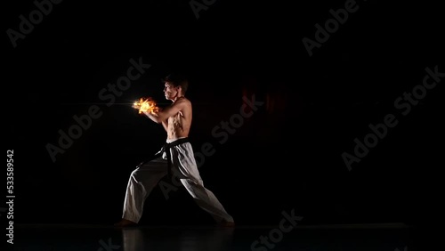 Male kyokushinkai karate performing kata on black studio background. Athlete delivers punches fists. Blows with the effect of 3D rendering of computer graphics in form yellow orange fire flames. photo
