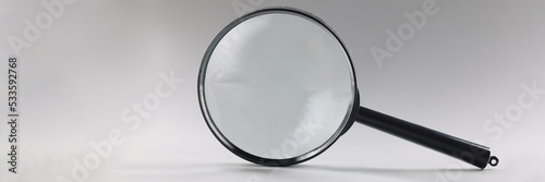 Single magnifying glass with black handle, leaning on grey surface