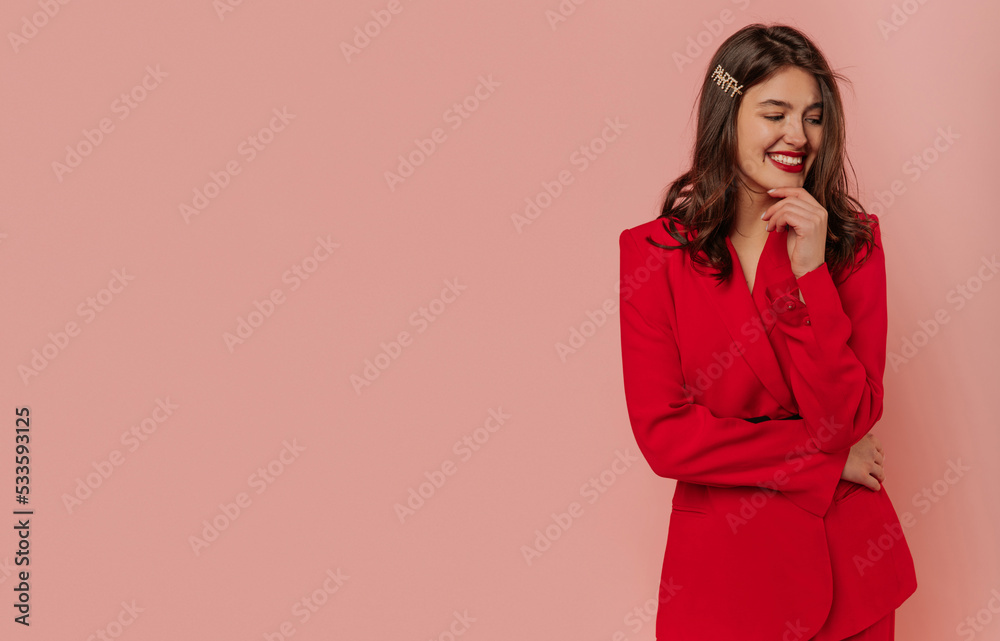 Smiling young caucasian girl with snow-white smile looks out over pink background. Brunette girl with wavy hair wears red jacket. Lifestyle, different emotions, leisure concept. Smiling young caucasian girl with snow-white smile looks out over pink background. Brunette girl with wavy hair wears red jacket. Lifestyle, different emotions, leisure concept.