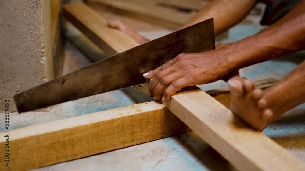 Male carpenter cutting wood plank with hand saw. Professional carpenter working at his workshop making home furniture. Woodworking and craftsmanship concept. Male carpenter cutting wood plank with hand saw. Professional carpenter working at his workshop making home furniture. Woodworking and craftsmanship concept.