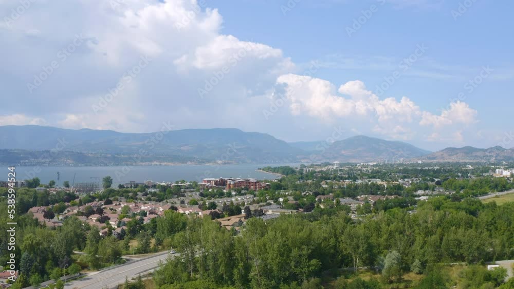 Aerial view of Kelowna homes in the suburbs on a sunny day, backing up to reveal fields and parks. Drone view. Aerial view of Kelowna homes in the suburbs on a sunny day, backing up to reveal fields and parks. Drone view.