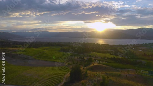 Aerial view of Kelowna wineries as the sun sets over the mountains across the Okanagan Lake. Drone.