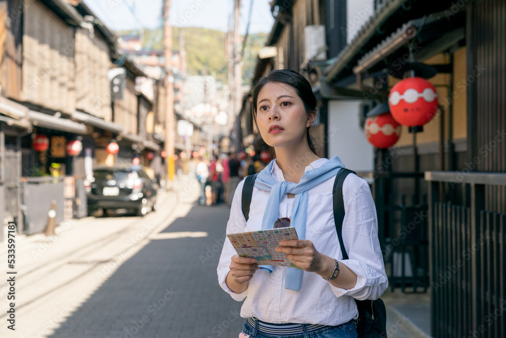 confused asian Japanese woman backpacker looking into distance and wondering which way to go while using map to find destination on Gion Hanamikoji Street in Kyoto japan - obrazy, fototapety, plakaty 
