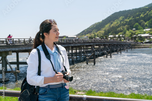 smiling asian Taiwanese woman traveler enjoying nice landscape by at riverside of Katsura River with Togetsu-kyo Bridge at background hile traveling to arashiyama in Kyoto japan on sunny day photo