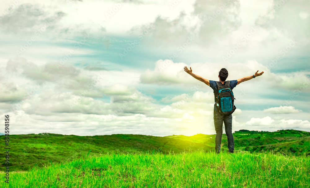 Man with backpack on a hill spreading his arms. Adventurous man spreading his arms in the countryside. Explorer man spreading his arms on a hill. Lifestyle of adventurous man in the field