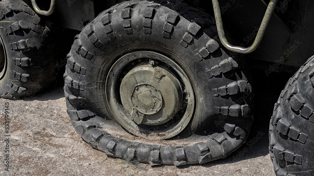 A punctured and flat tire of military equipment of the armored personnel carrier. Military conflict, the shelling of the wheel.