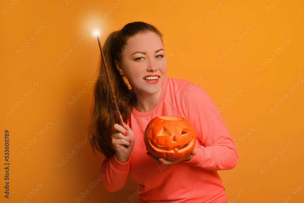 Happy young woman holding luminous magic wand or glowing magic stick with carved Halloween pumpkin or Jack o lantern pumpkin and looking at camera on yellow background.
Smiling girl is conjuring. Happy young woman holding luminous magic wand or glowing magic stick with carved Halloween pumpkin or Jack o lantern pumpkin and looking at camera on yellow background.
Smiling girl is conjuring.