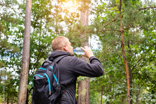 A man drinks water in the forest on a summer sunny day. Survival in the forest, dehydration of the body.