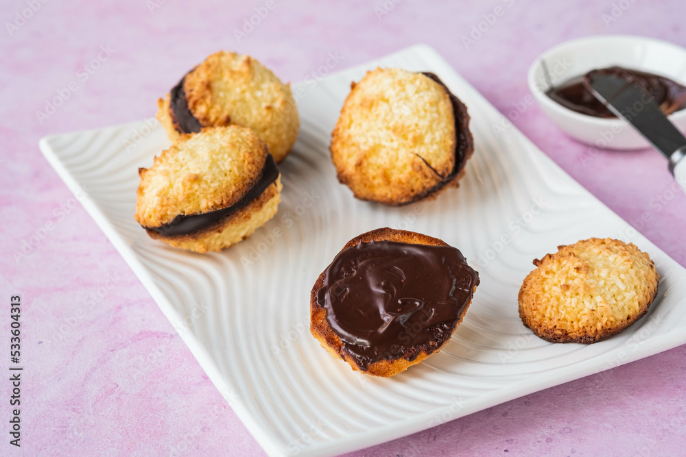Dessert, coconut cookies with dark chocolate on a white rectangular plate on a pink concrete background. Dessert, coconut cookies with dark chocolate on a white rectangular plate on a pink concrete background.