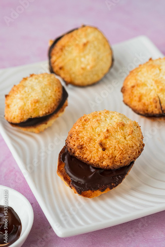 Dessert, coconut cookies with dark chocolate on a white rectangular plate on a pink concrete background.