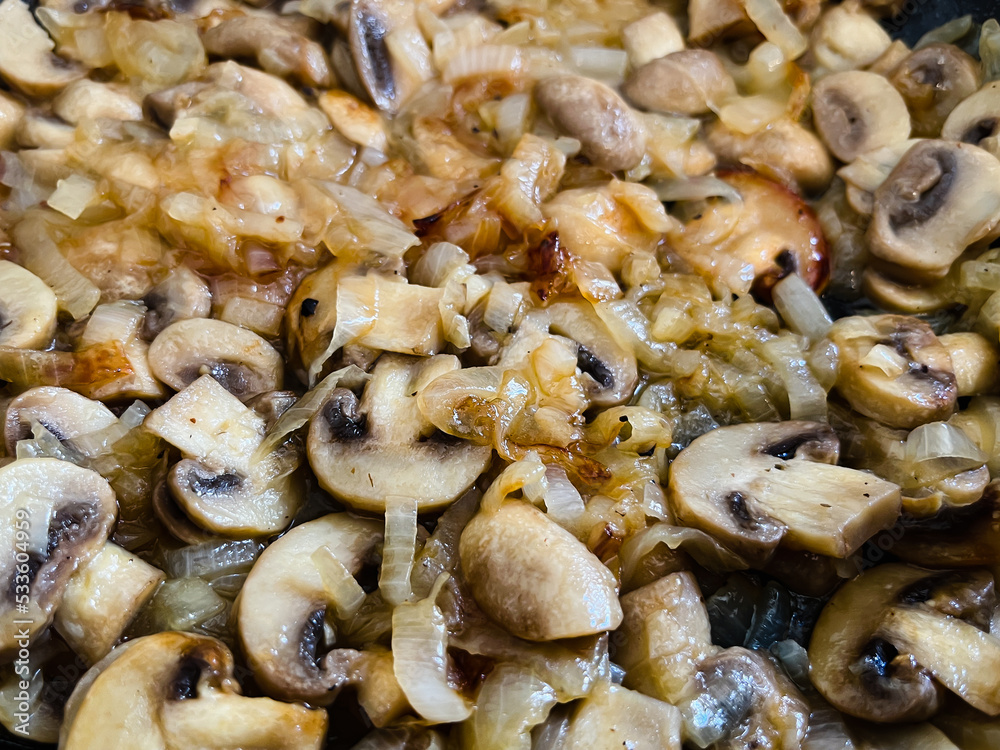 White champignon mushrooms are fried with onions in a frying pan. White champignon mushrooms are fried with onions in a frying pan.